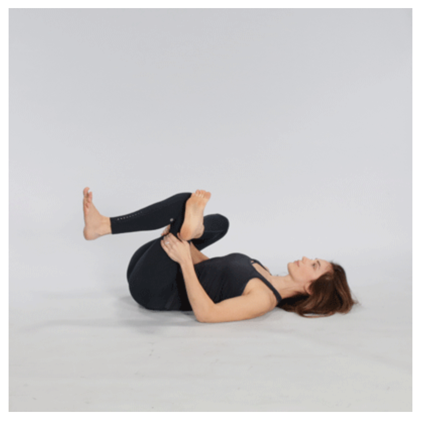 A woman performing the figure-4 stretch, using her left leg crossed over her right knee while sitting on the ground. This stretch helps in stretching the piriformis muscle